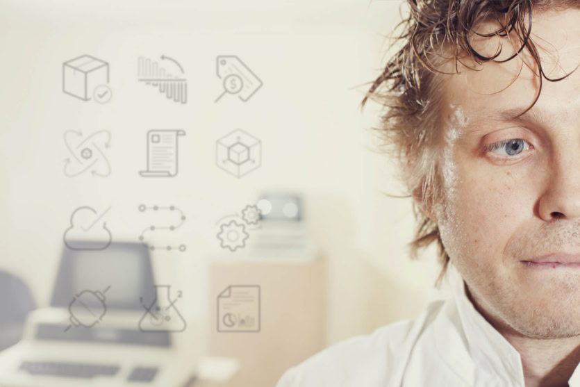 A man wearing a white lab coat stands in front of blurred office equipment and floating data-related icons, highlighting innovation amidst the backdrop of a legacy system.